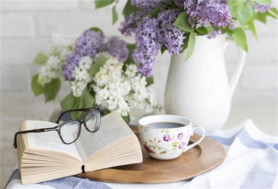 Open book with glasses, lilacs and a cup of coffee.