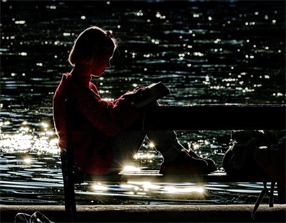 Girl reading while backlit by sparkling water.