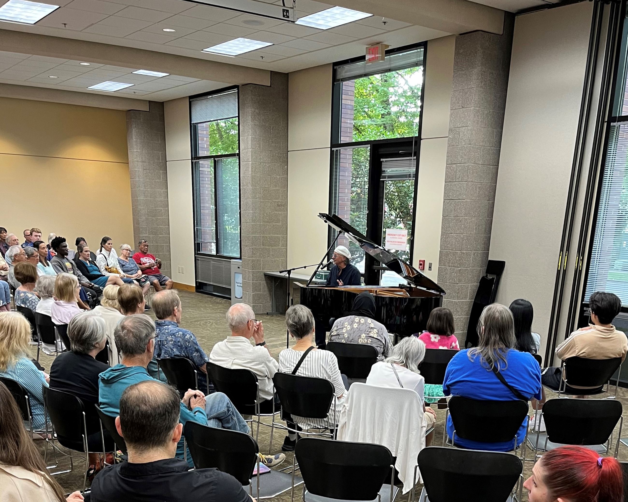 Pianist at a piano in a room full of people seated in an arc.