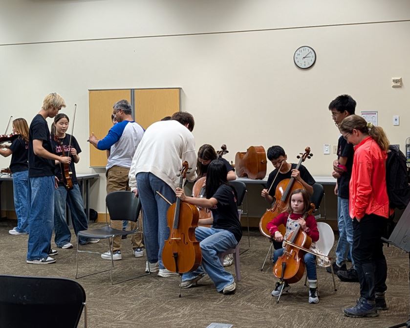 Children and caregivers standing or sitting with musical instruments, trying them out.