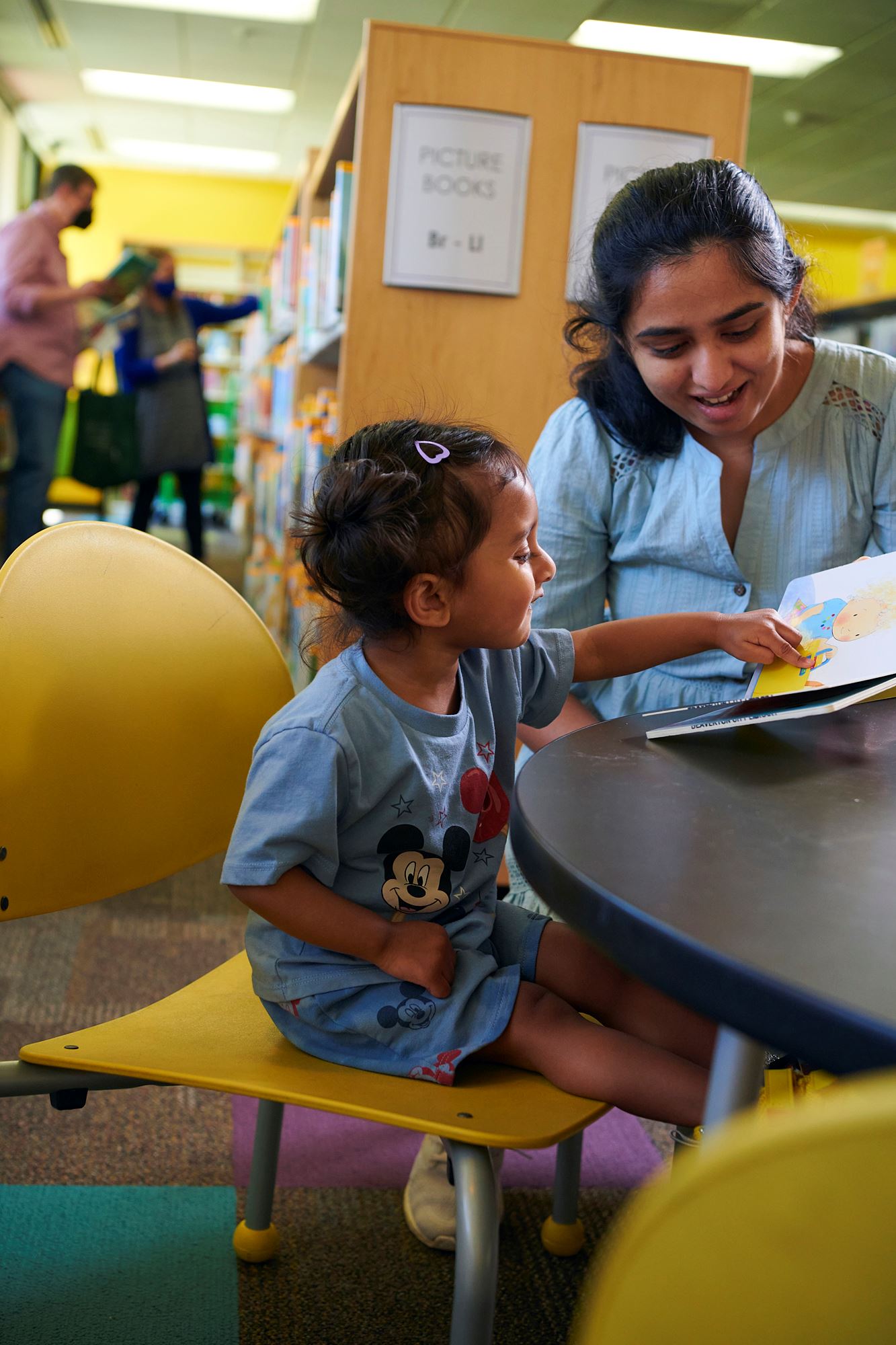Photo of a woman reading a book with a small child in a library.