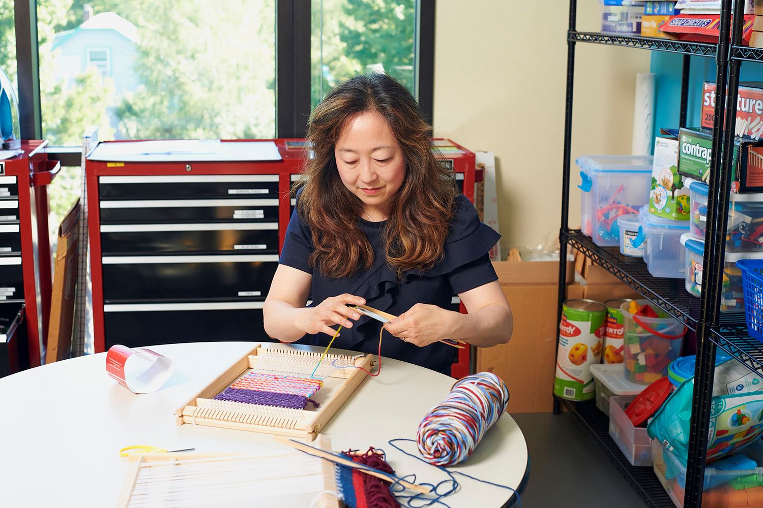 A woman in a library makerspace using a tabletop loom to create a colorful weaving.